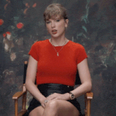 a woman in a red shirt and black skirt sits in a director 's chair
