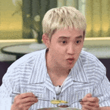 a man in a striped shirt is eating food with a fork and spoon .