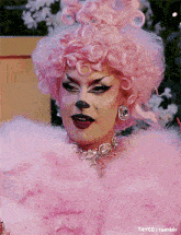 a drag queen wearing a pink wig and feathers looks at the camera