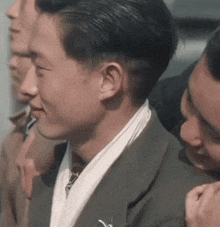 a man in a suit and tie with a scarf around his neck is talking to another man .