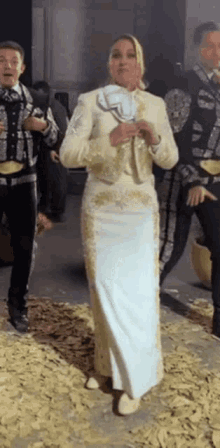 a woman in a white dress is standing in front of a group of mariachi singers .