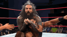 a man with dreadlocks is wrestling another man in a wrestling ring with a crowd watching