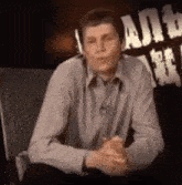 a man is sitting in a chair with his hands folded .