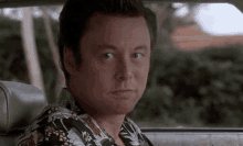 a man in a hawaiian shirt is sitting in the back seat of a car .