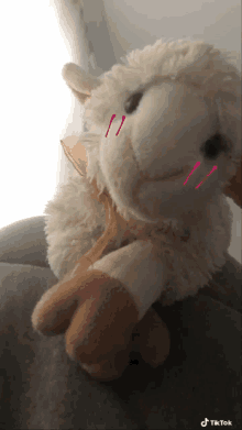 a stuffed sheep with a bow around its neck is sitting on a couch with tiktok written on the bottom