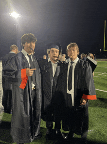 three graduates pose for a photo on a field