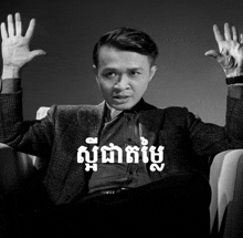 a man in a suit is sitting in a chair with his hands in the air and a black and white photo with foreign writing on it