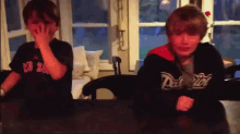 a boy wearing a red sox shirt covers his face while another boy wearing a patriots jacket covers his face