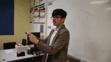 a man in a plaid jacket stands in front of a white board holding a pen