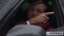 a man sitting in a car pointing out the window with kapwing written on the bottom