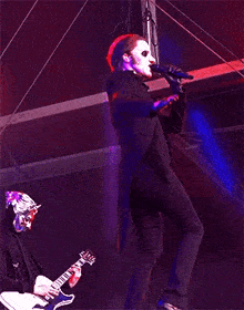a man in a mask is singing into a microphone while standing on a stage .
