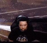 a man with a beard is sitting in a chair wearing headphones and a black shirt .
