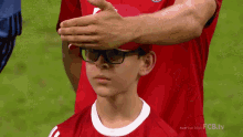 a young boy wearing glasses and a red shirt with fcb.tv on the bottom