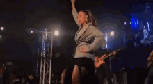 a woman is singing into a microphone on a stage while a man plays a guitar in the background .