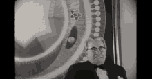 a black and white photo of a man in a tuxedo standing in front of a picture .