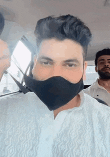 a man wearing a black face mask is sitting in a car with two other men