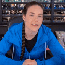 a woman in a blue jacket is sitting in front of a shelf full of cosmetics