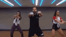 a man and two women are dancing together in a gym under neon lights .