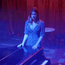 a woman in a blue dress stands in front of a piano in a dark room