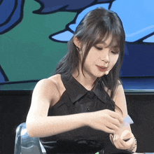 a woman in a black dress is sitting at a table with a microphone in her hand