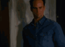 a man in a denim shirt is standing in front of a door and looking down .