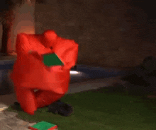 a person in a red inflatable suit is laying on the grass next to a swimming pool .