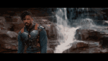 a man standing in front of a waterfall wearing a blue shirt