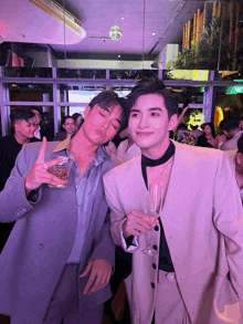 two men standing next to each other with one holding a glass of beer and the other holding a glass of champagne