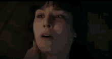 a close up of a woman 's face in a dark room with a hand touching her face .