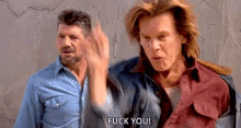 two men are standing next to each other and one of them is giving a middle finger .