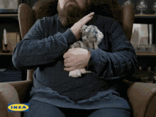 a man with a beard is sitting in a chair holding a stuffed animal with ikea written on the bottom