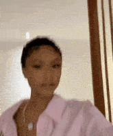 a woman wearing a pink shirt and a necklace is standing in front of a door .