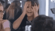 a woman is covering her face with her hands while sitting in front of a mirror .