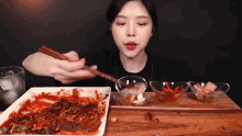 a woman eating a plate of food with chopsticks and a glass of water