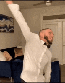 a man in a bow tie is dancing in a living room with his arms in the air .