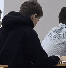 a man in a black hoodie is sitting in a classroom with other students .