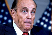 a man in a suit and tie is making a funny face in front of an american flag