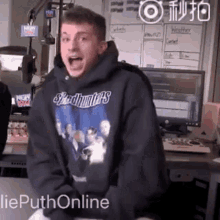 a young man wearing a speedhunters sweatshirt is standing in front of a computer .