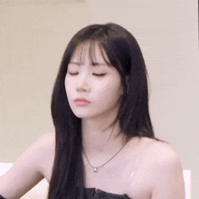 a young woman with long black hair is wearing a strapless top and a necklace .