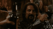a man with long hair is smoking a cigarette while another man holds a gun .
