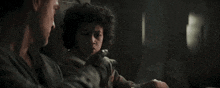 a man and a young boy are sitting next to each other in a dark room . the boy is holding a gun .
