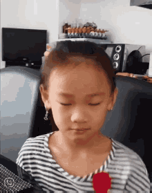 a little girl with her eyes closed is wearing a striped shirt and earrings