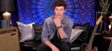 a young man is sitting on a couch next to a guitar .
