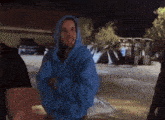 a man wearing a blue hoodie is standing in a parking lot
