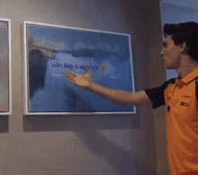 a man in an orange shirt is touching a framed painting that says win like a winner