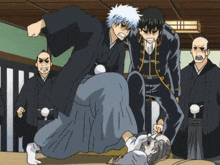 a group of men in kimonos are standing around a man laying on the floor