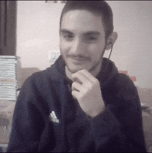a young man wearing a black adidas sweatshirt looks at the camera