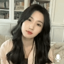 a young woman with long black hair is sitting on a couch in front of a microphone .