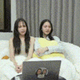 two women are sitting on a couch looking at a laptop computer