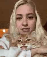 a blonde woman is holding an orange and white cat with her mouth open